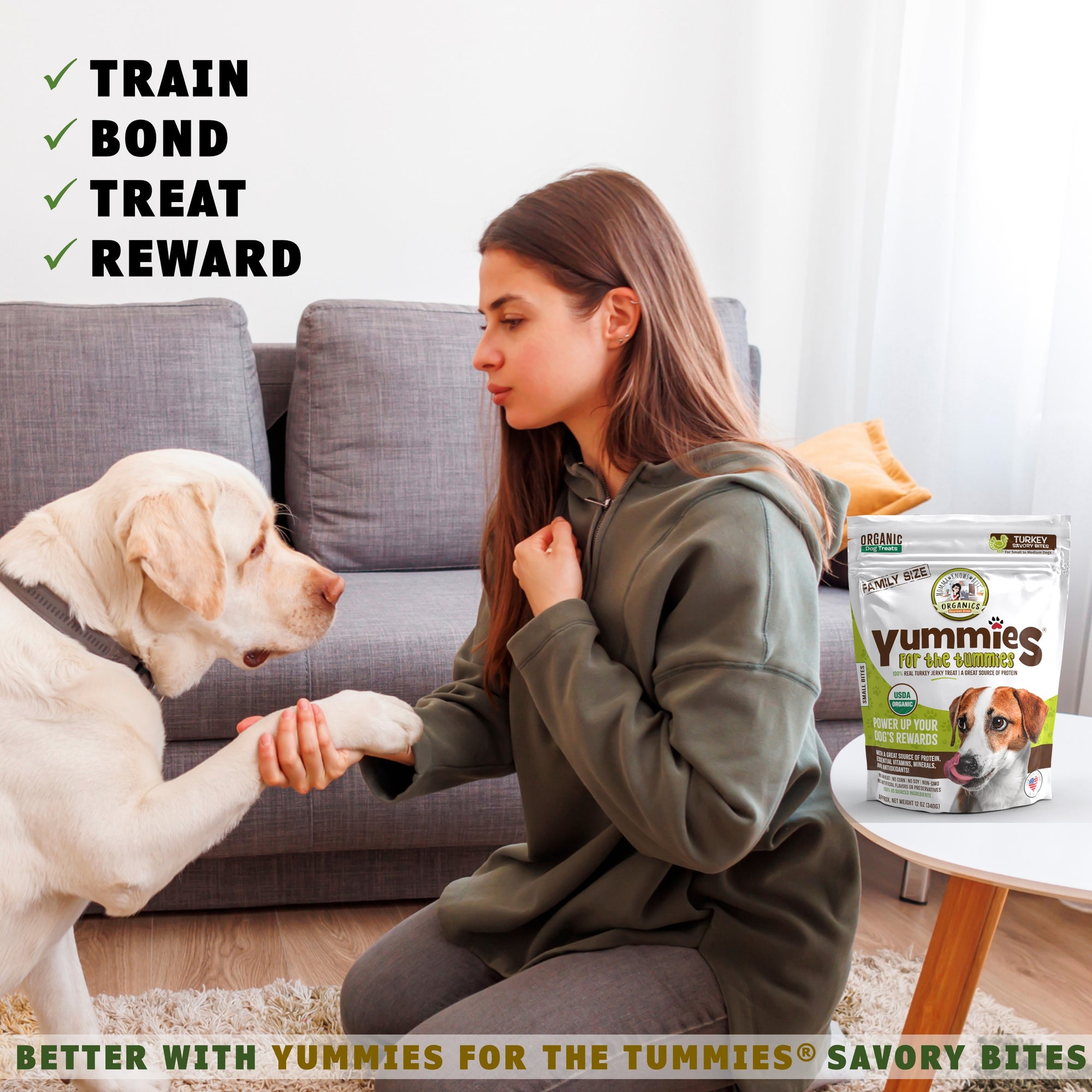 A person sitting on the floor with a dog next to a bag of organic dog turkey treats yummies for the tummies by momma knows best organics 
